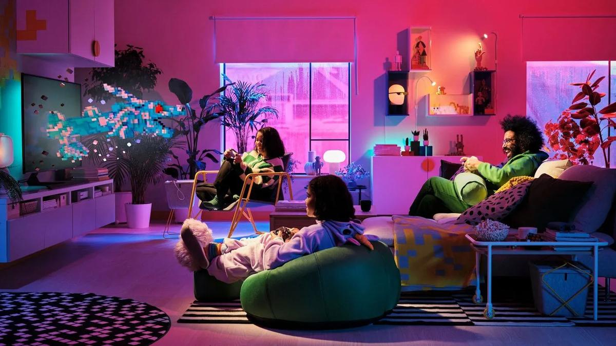 Three people gaming in a cozy, colorful living room with vibrant lighting and pixelated art on the wall.