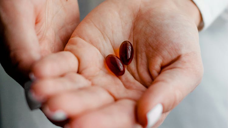 A hand holding two brown pills